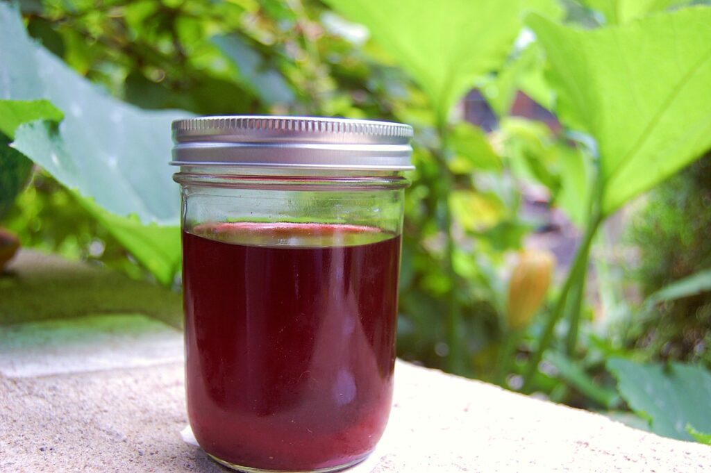 A mason jar of dark pink liquid sits on a porch wall